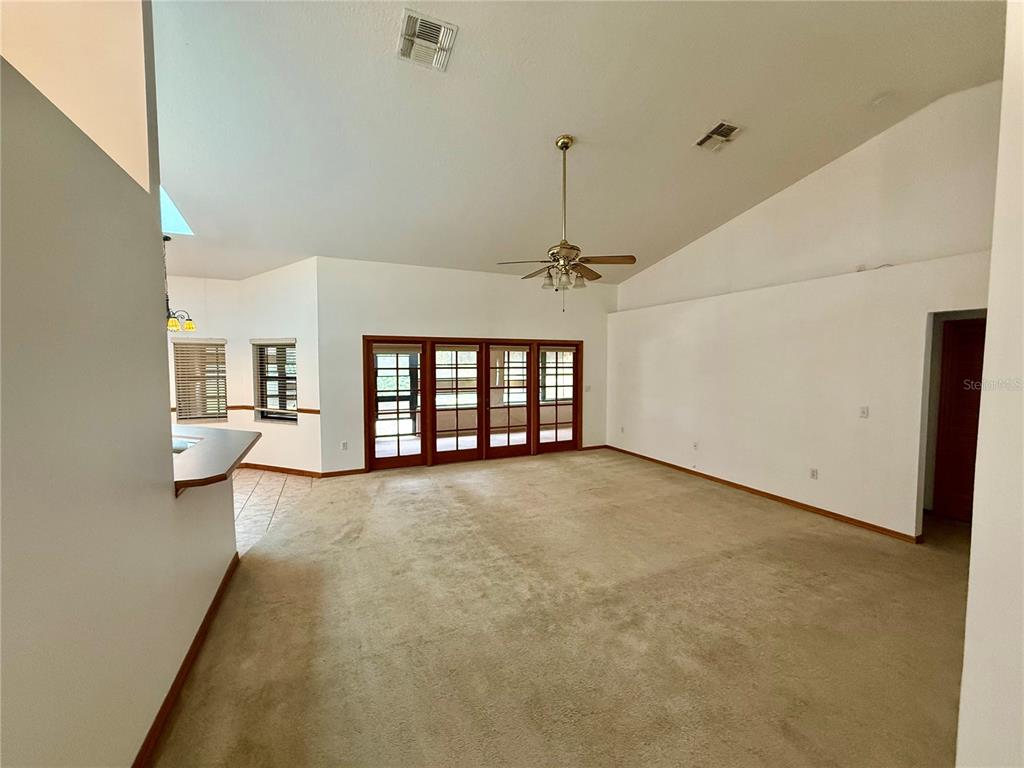 A spacious living room features beige carpeting, a vaulted ceiling, and sliding glass doors — 4843 CALASANS AVENUE, ST CLOUD, FL