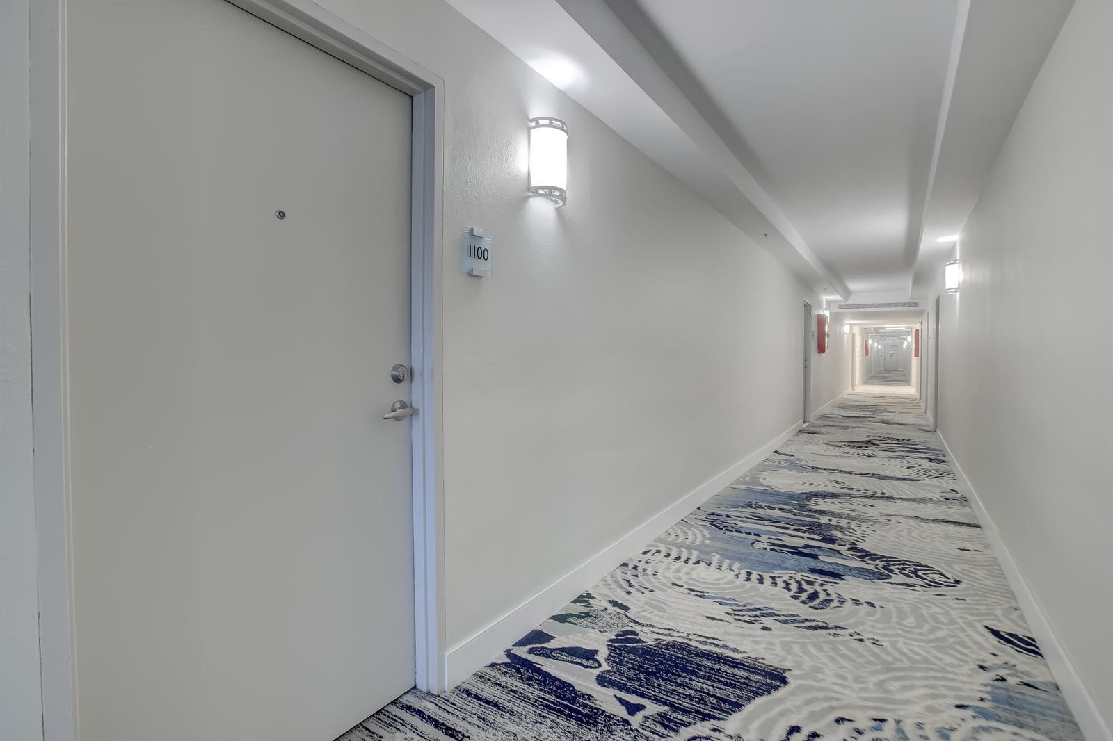 A long hotel hallway features white walls, patterned blue and grey carpet, and room 1100 — 3000 S Ocean Drive # 1100, Hollywood FL 33019, HOLLYWOOD, FL