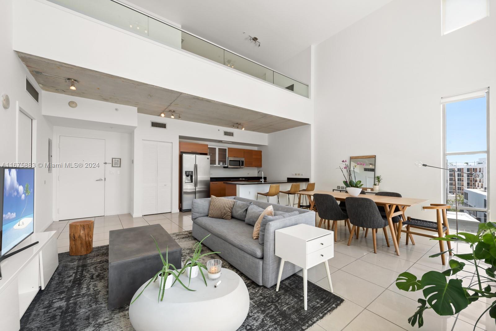 A modern open-concept living and dining area features high ceilings, concrete accents, and tile flooring — 3449 NE 1 AVE # L61, Miami FL 33137, MIAMI, FL