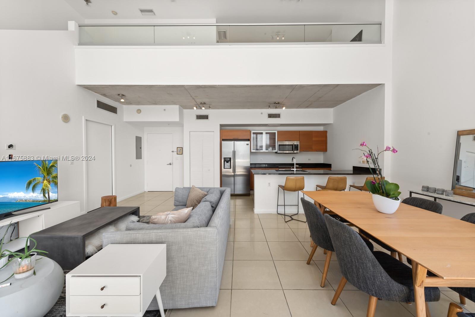 An open-concept living and dining area features a modern kitchen, concrete ceiling, and loft level — 3449 NE 1 AVE # L61, Miami FL 33137, MIAMI, FL