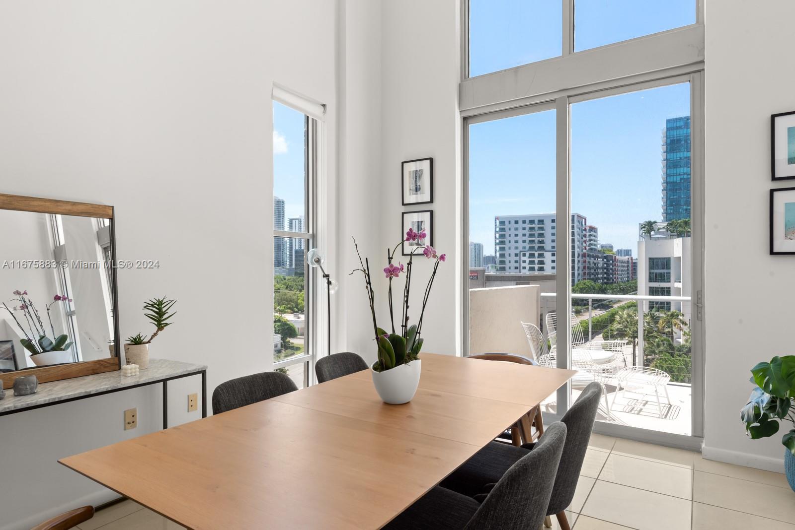 A dining room features a wooden table, grey chairs, and floor-to-ceiling windows with balcony access — 3449 NE 1 AVE # L61, Miami FL 33137, MIAMI, FL