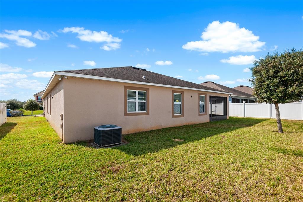 The exterior of a tan stucco house features a backyard, an air conditioning unit, and windows — 236 BARRINGTON DRIVE, HAINES CITY, FL