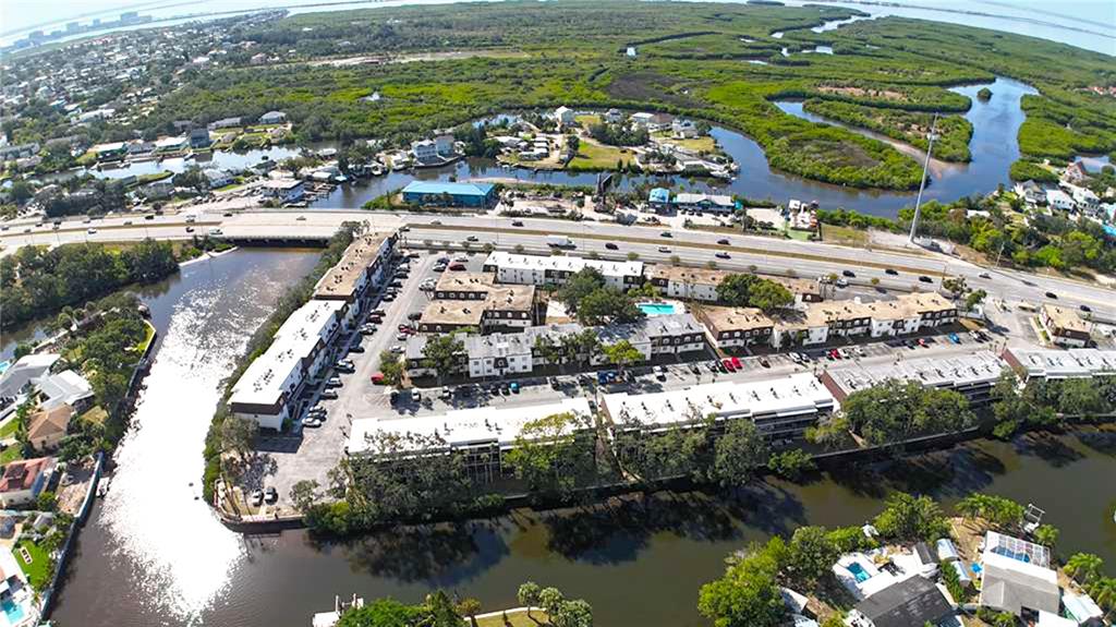 An aerial view shows a multi-building apartment complex situated along a waterway near a highway — 9002 TUDOR DRIVE UNIT K201, TAMPA, FL