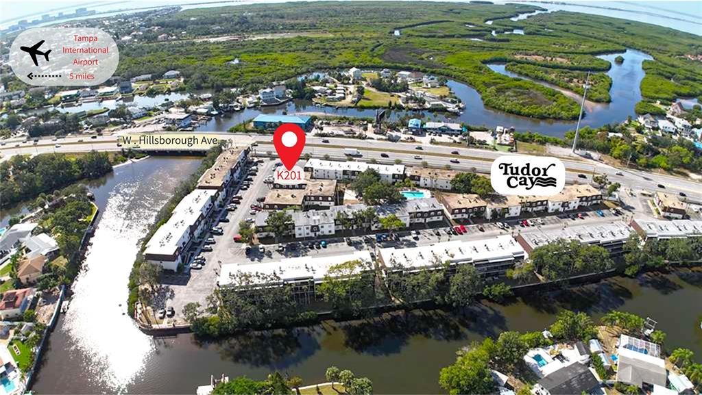 This aerial view shows a multi-building apartment complex situated along a waterway near a highway — 9002 TUDOR DRIVE UNIT K201, TAMPA, FL