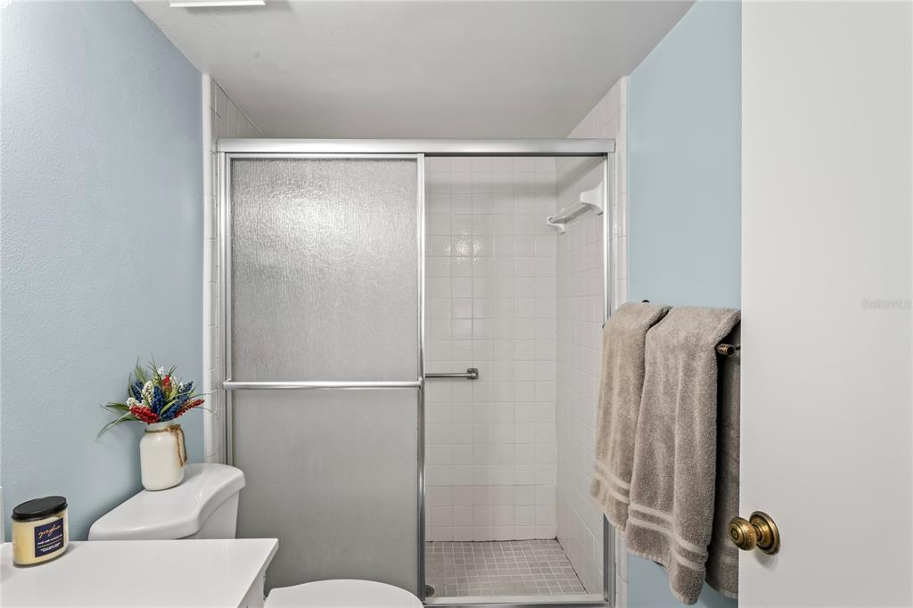 A bathroom features a tiled walk-in shower with sliding glass doors and light blue walls — 3232 LAKE PINE WAY E UNIT H2, TARPON SPRINGS, FL