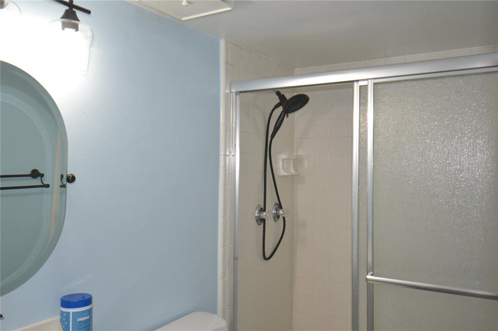 A bathroom features a light blue wall, a circular mirror, and a tiled walk-in shower — 3232 LAKE PINE WAY E UNIT H2, TARPON SPRINGS, FL