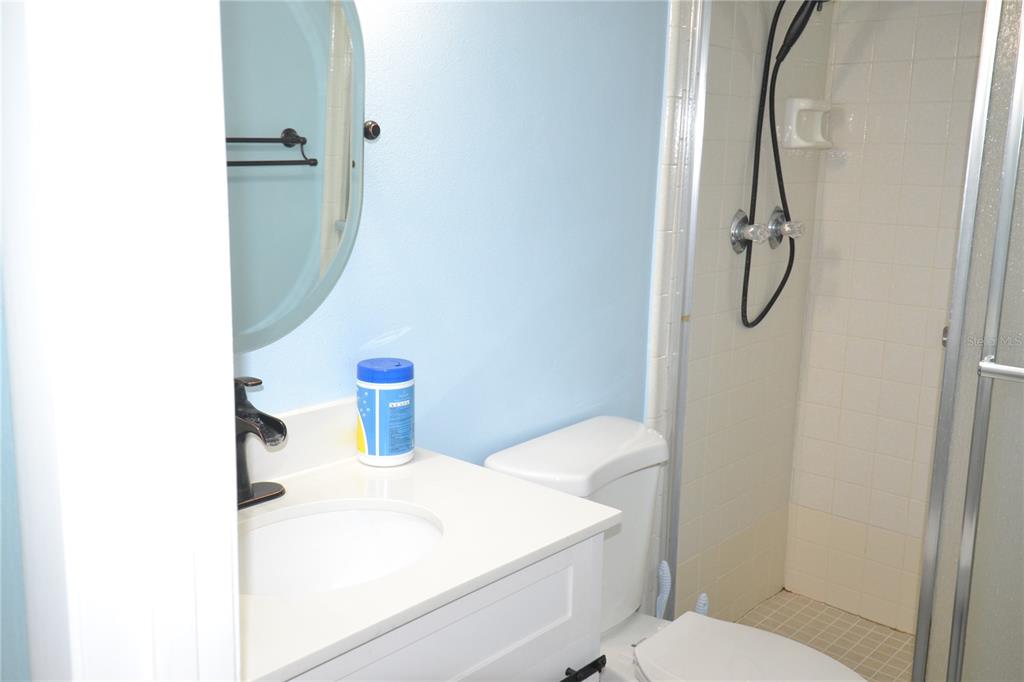 A bathroom features a white vanity, a round mirror, a toilet, and a tiled shower — 3232 LAKE PINE WAY E UNIT H2, TARPON SPRINGS, FL