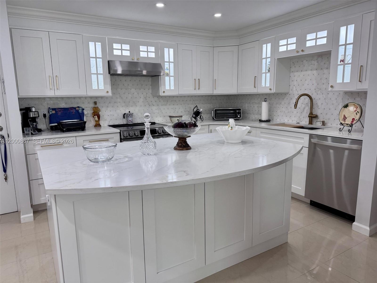 A white kitchen features a curved marble island, stainless steel appliances, and a tiled backsplash — 10850 N Kendall Dr # 414, Miami FL 33176, MIAMI, FL