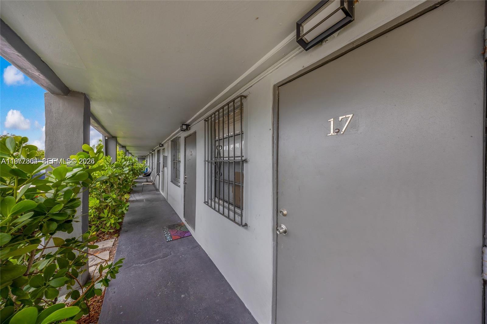 An exterior walkway features a row of gray apartment doors with security bars on windows — 5807 SW 25th St # 18, West Park FL 33023, WEST PARK, FL