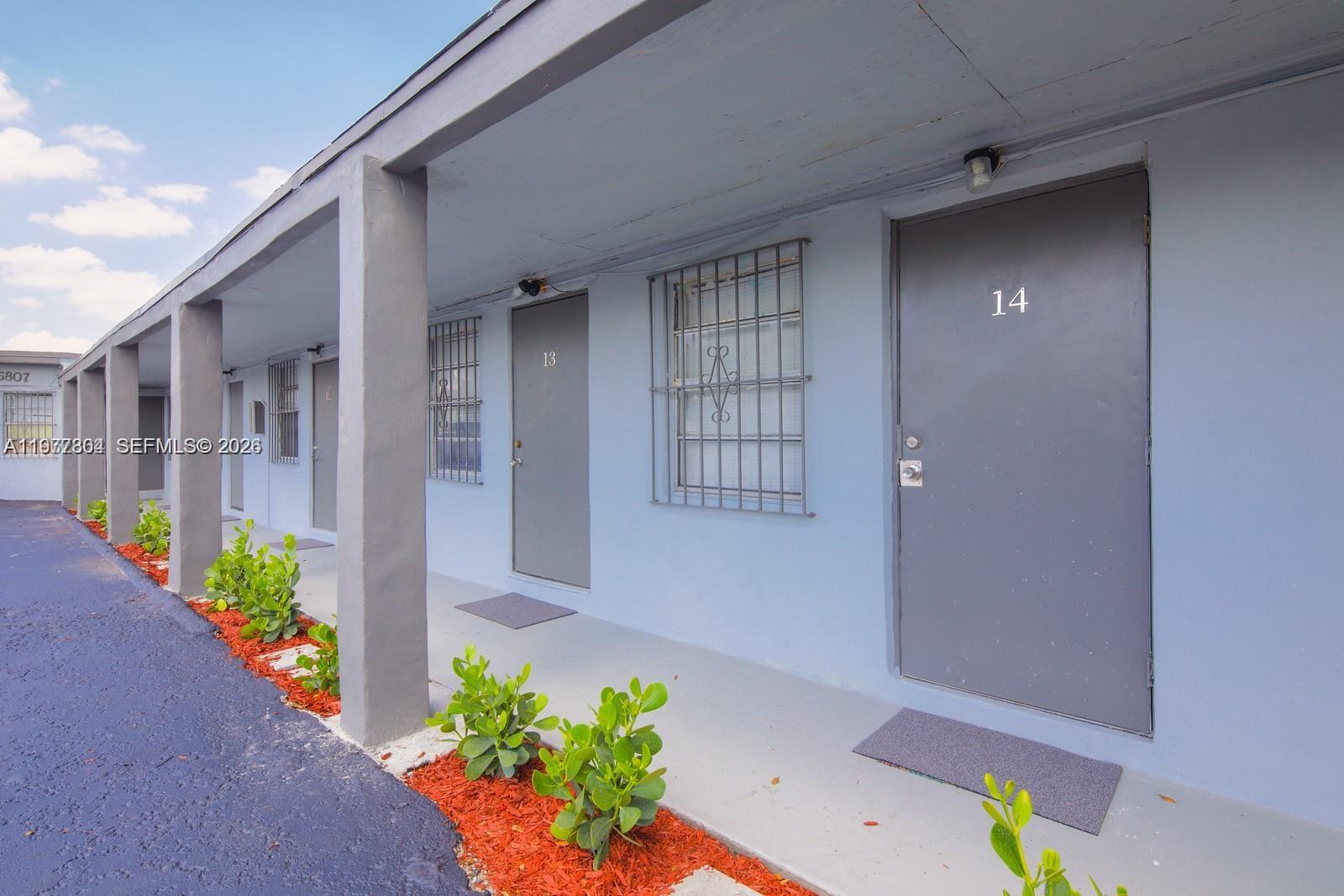 A row of light blue apartment units features gray doors, security bars on windows, and landscaping — 5807 SW 25th St # 18, West Park FL 33023, WEST PARK, FL