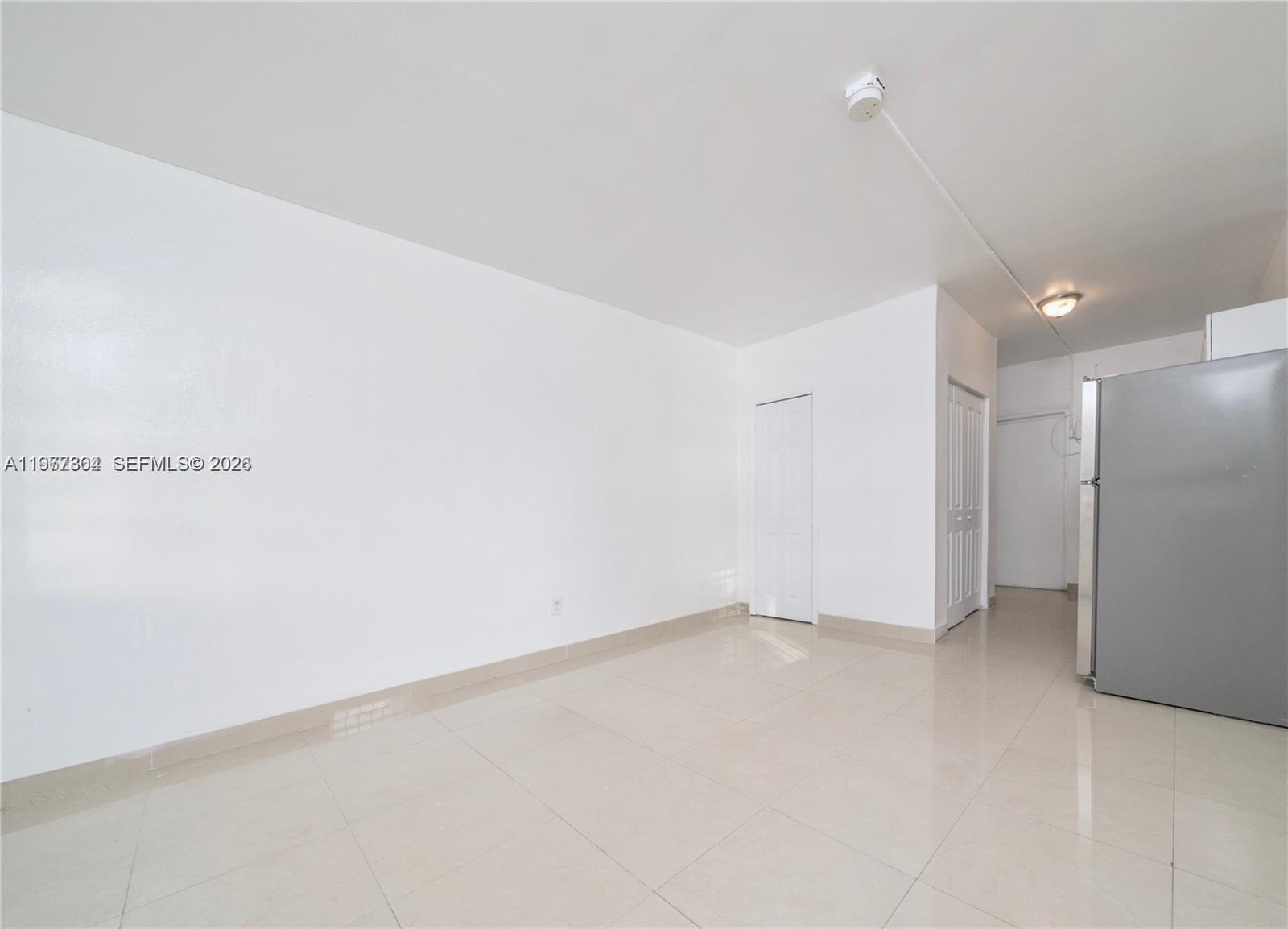 A bright room features white walls, light-colored tile flooring, and a stainless steel refrigerator — 5807 SW 25th St # 18, West Park FL 33023, WEST PARK, FL