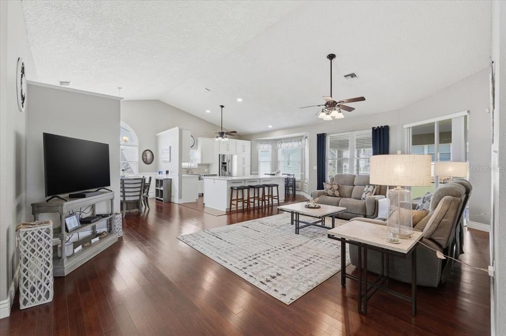 An open-concept living room and kitchen with hardwood floors, vaulted ceilings, and neutral decor — 5832 SWALLOW DRIVE, LAKELAND, FL