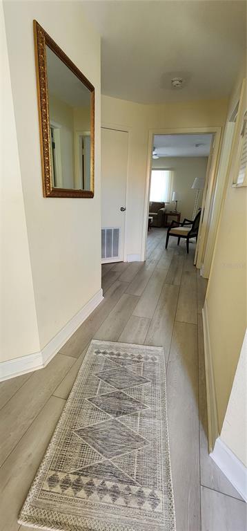A hallway with light-colored wood-look flooring, a patterned runner rug, and a wall-mounted mirror — 1515 PINELLAS BAYWAY S UNIT 8, TIERRA VERDE, FL