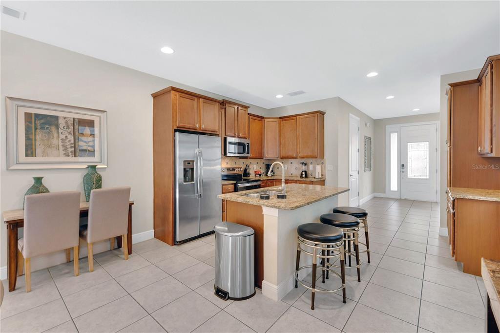 A kitchen features wood cabinets, granite countertops, a center island with stools, and tile flooring — 410 NOVI PATH, KISSIMMEE, FL