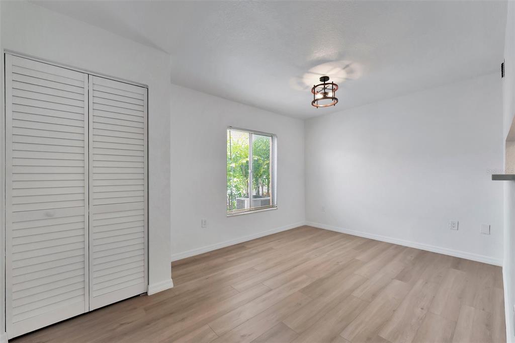 An empty bedroom features white walls, light wood-look flooring, a closet, and a ceiling light — 9940 7TH WAY N UNIT 101, ST PETERSBURG, FL