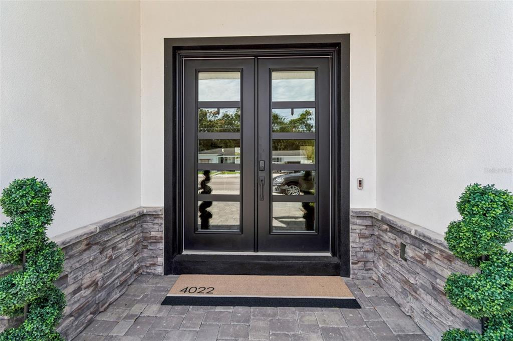 A black double front door with glass panels is flanked by stone veneer and topiary trees — 4022 W BAY TO BAY BOULEVARD, TAMPA, FL