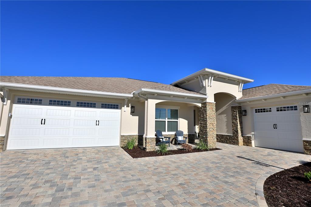 A beige house exterior features a stone-accented entryway, two white garage doors, and paver driveway — 10555 SW 96TH LANE ROAD, OCALA, FL