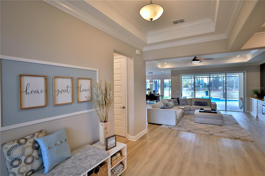 A foyer with a bench and wall art leads into a living room with pool views — 10555 SW 96TH LANE ROAD, OCALA, FL