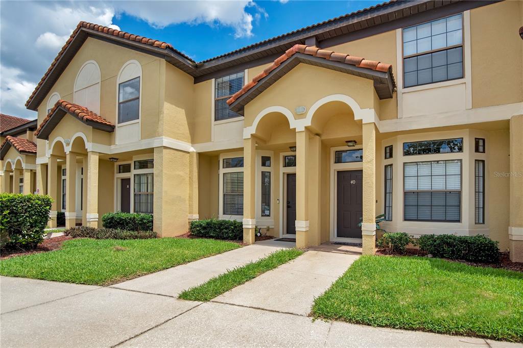 A two-story townhouse exterior features tan stucco walls, arched entryways, and a tiled roof — 6007 SCOTCHWOOD GLEN UNIT 39, ORLANDO, FL