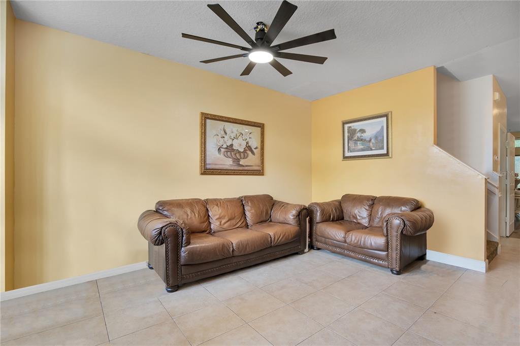 A living room with yellow walls, tile flooring, two brown leather sofas, and a ceiling fan — 6007 SCOTCHWOOD GLEN UNIT 39, ORLANDO, FL