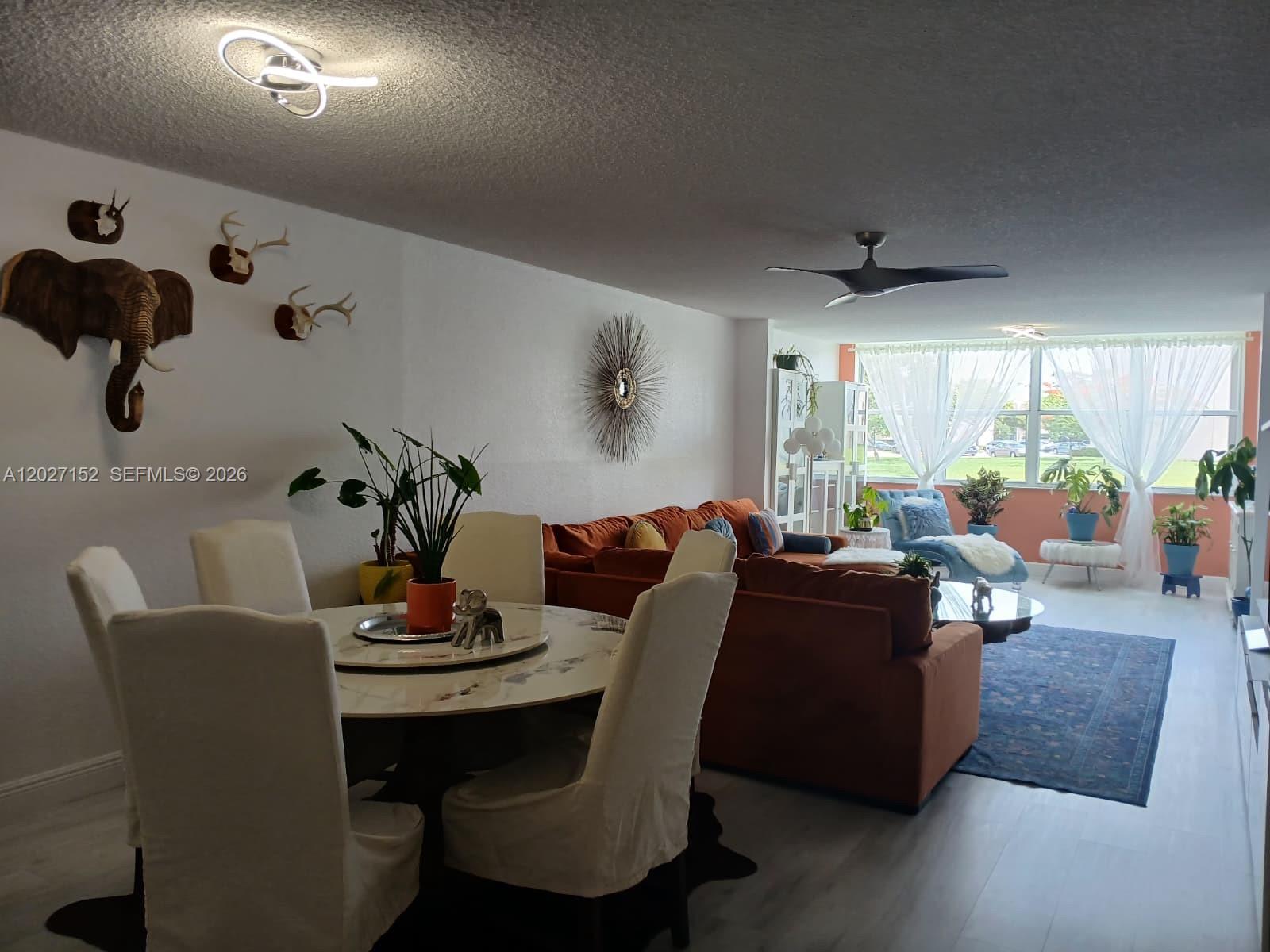 A dining area and living room feature white walls, a large orange sofa, and plants — 2603 NW 103rd Ave # 110, Sunrise FL 33322, SUNRISE, FL