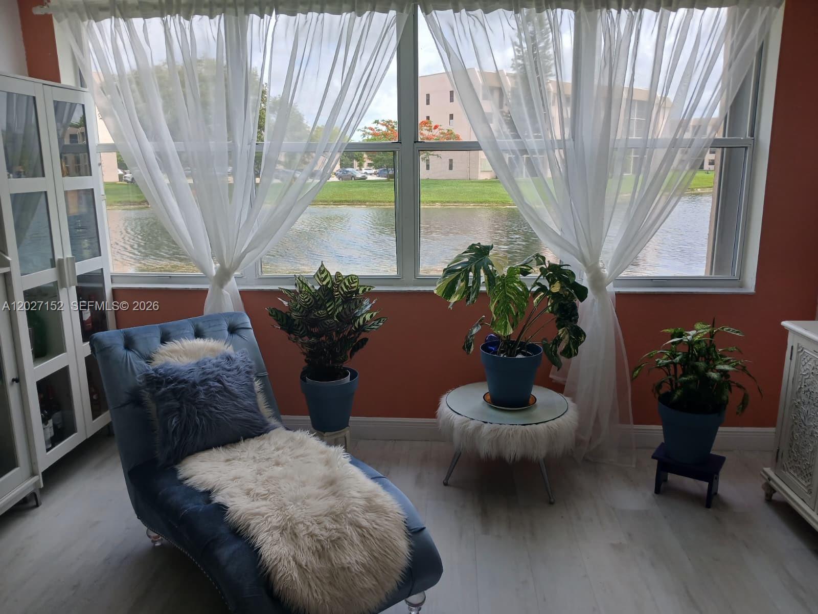 A sunroom features a blue chaise lounge, potted plants, and large windows overlooking a lake — 2603 NW 103rd Ave # 110, Sunrise FL 33322, SUNRISE, FL