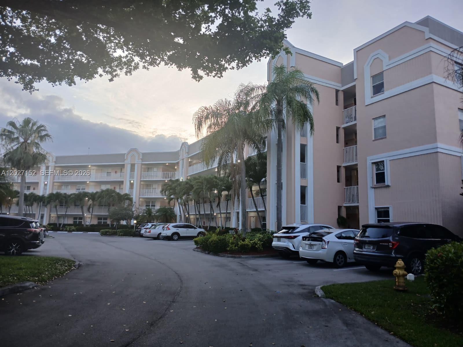 An exterior view of a multi-story apartment building with a parking lot and palm trees — 2603 NW 103rd Ave # 110, Sunrise FL 33322, SUNRISE, FL