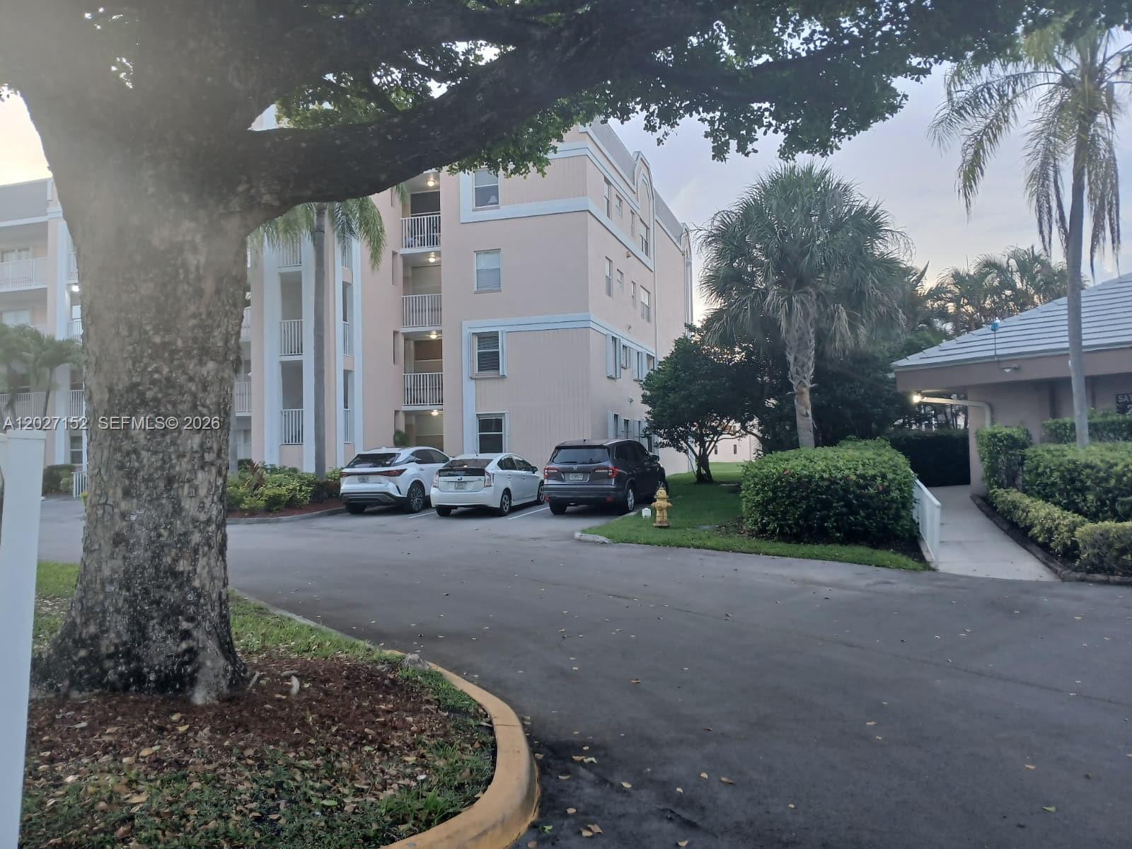 A multi-story apartment building with parked cars sits behind a large tree and landscaping — 2603 NW 103rd Ave # 110, Sunrise FL 33322, SUNRISE, FL