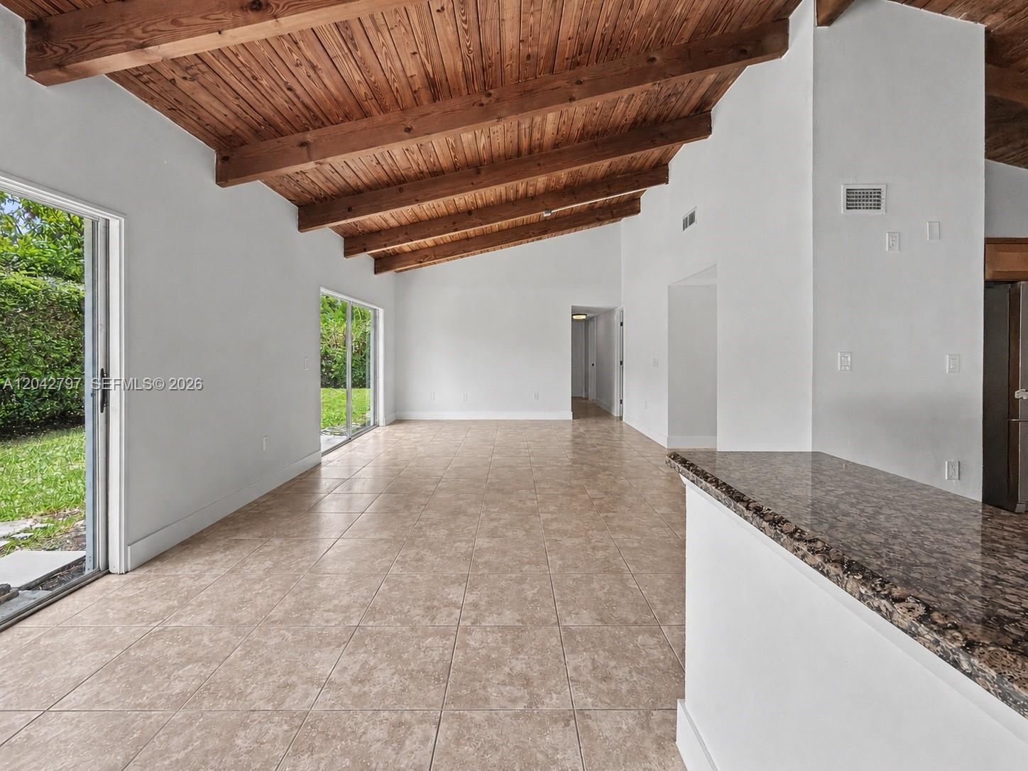 An open-concept living area features a vaulted wood-beam ceiling, tile flooring, and sliding glass doors — 10262 SW 127th Pl, Miami FL 33186, MIAMI, FL
