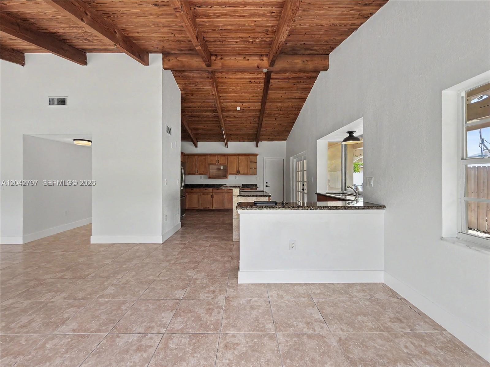 A kitchen with wood-beamed ceilings and tile flooring opens to a living area — 10262 SW 127th Pl, Miami FL 33186, MIAMI, FL