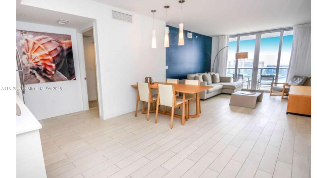An open-concept living and dining area features light wood-look tile floors and a blue accent wall — 2602 E Hallandale Beach Blvd # R2010, Hallandale Beach FL 33009, HALLANDALE BEACH, FL