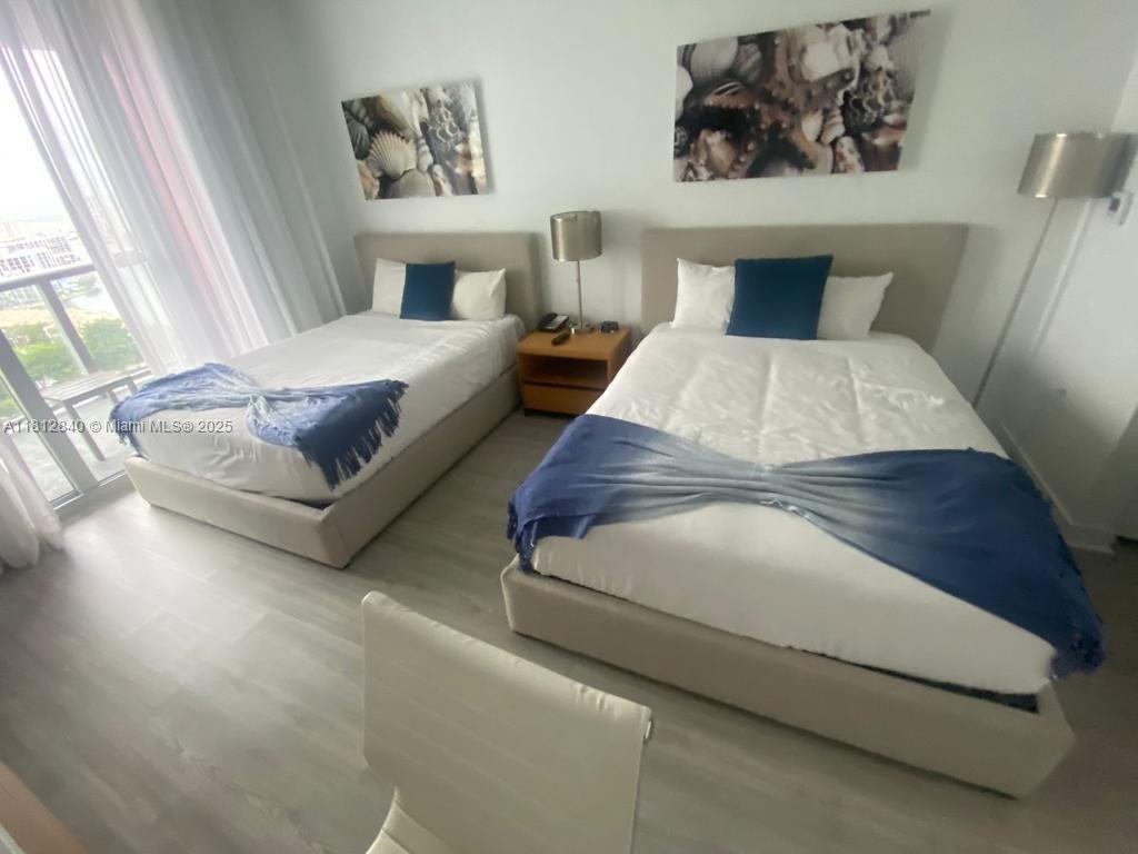 A bedroom features two beds with blue accents, light wood flooring, and coastal wall art — 2602 E Hallandale Beach Blvd # R2010, Hallandale Beach FL 33009, HALLANDALE BEACH, FL