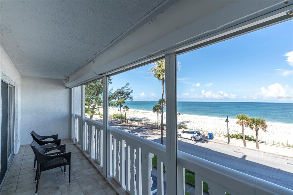 A screened balcony with tiled flooring overlooks a beach, a road, and the ocean — 403 GULF WAY UNIT 302, ST PETE BEACH, FL