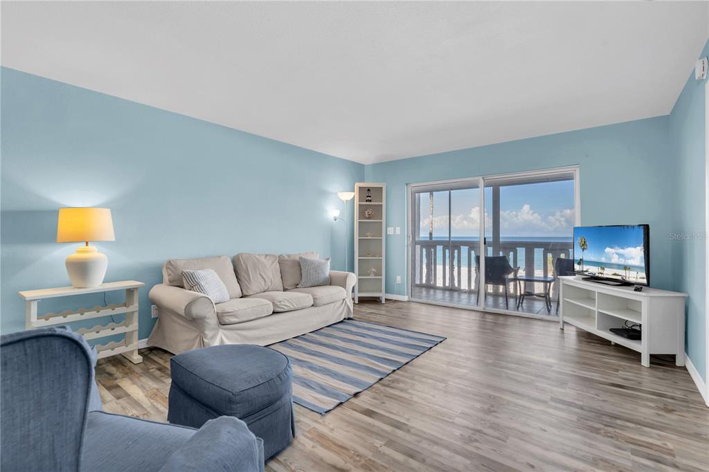 A living room with light blue walls, a beige sofa, and a balcony overlooking the ocean — 403 GULF WAY UNIT 302, ST PETE BEACH, FL