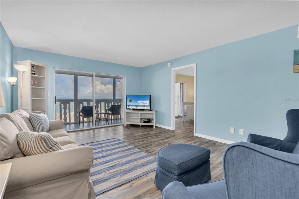 A living room with light blue walls, wood-look flooring, a beige sofa, and a balcony view — 403 GULF WAY UNIT 302, ST PETE BEACH, FL