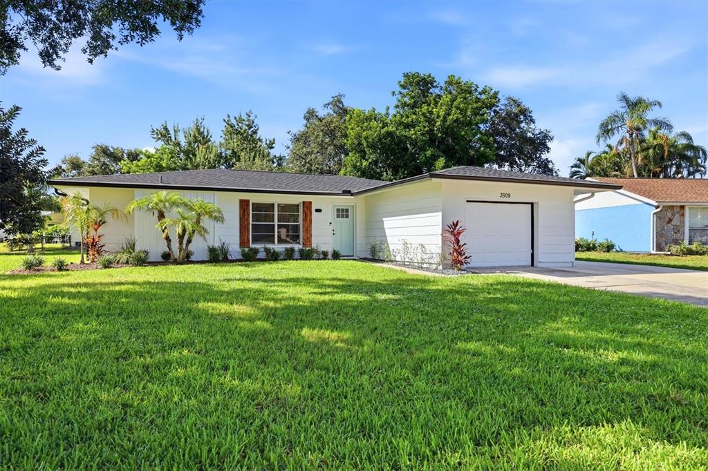 A single-story house with white siding, a garage, and a green lawn under a blue sky — 3509 64TH STREET W, BRADENTON, FL