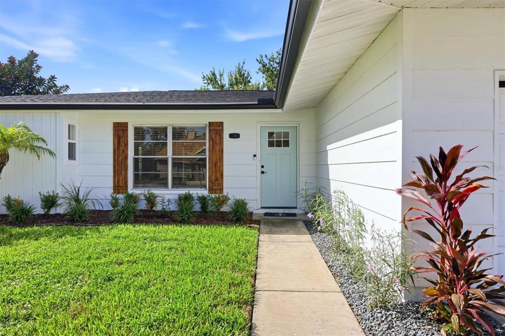 A white house exterior features a light blue front door, wood shutters, and a concrete walkway — 3509 64TH STREET W, BRADENTON, FL