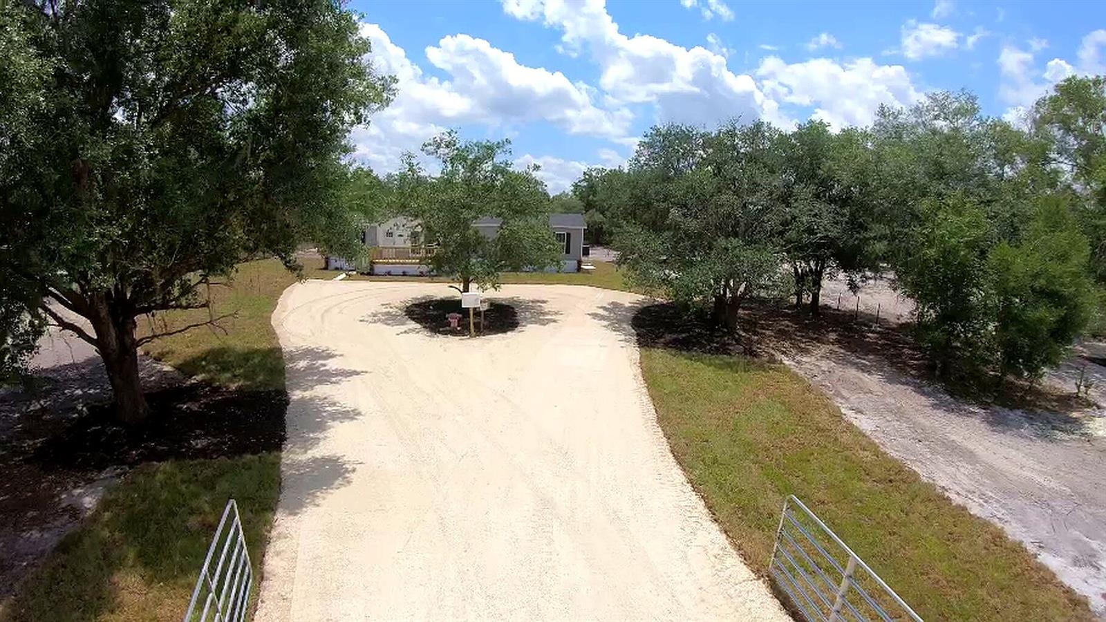 A gray manufactured home with a wooden deck sits beside a large gravel driveway — 18574 NW 284th Street, Okeechobee FL 34972, OKEECHOBEE, FL