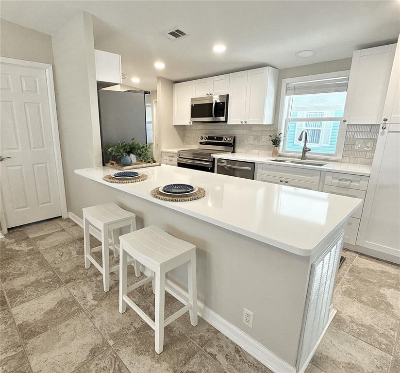 A kitchen features white cabinets, a quartz island with two stools, and stainless steel appliances — 7107 MOUNT ESSEX DRIVE NE UNIT 520, ST PETERSBURG, FL