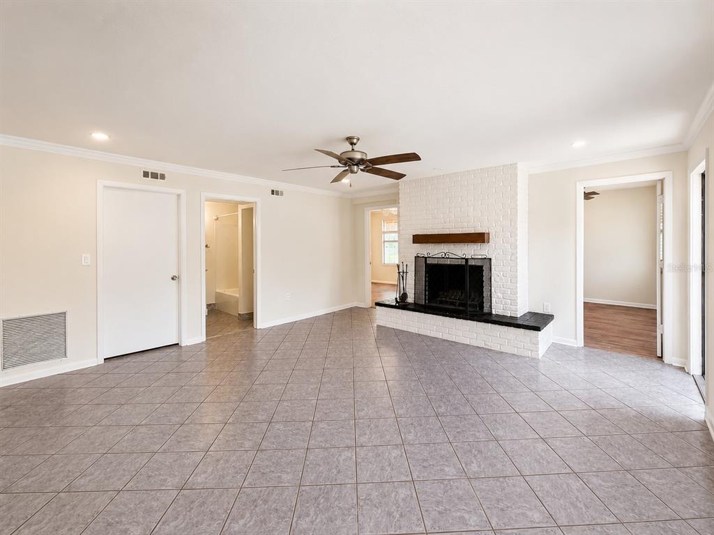 A living room with light tile flooring, a white brick fireplace, and a ceiling fan — 7301 N DARTMOUTH AVENUE, TAMPA, FL