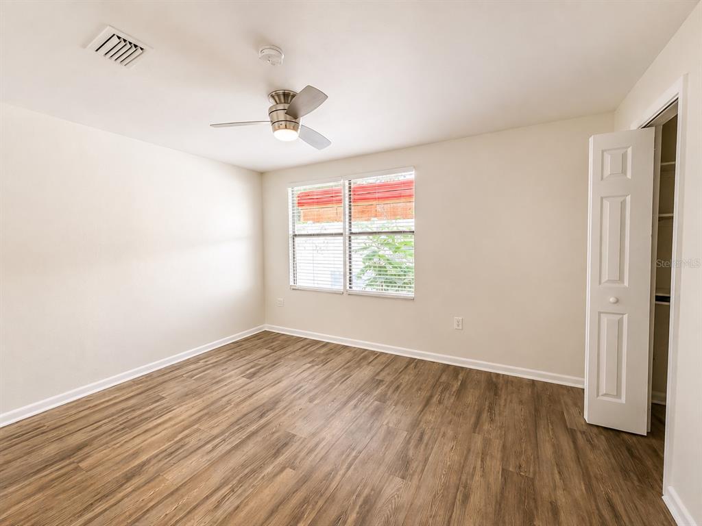 An empty bedroom features light-colored walls, wood-look flooring, a ceiling fan, and a closet — 7301 N DARTMOUTH AVENUE, TAMPA, FL