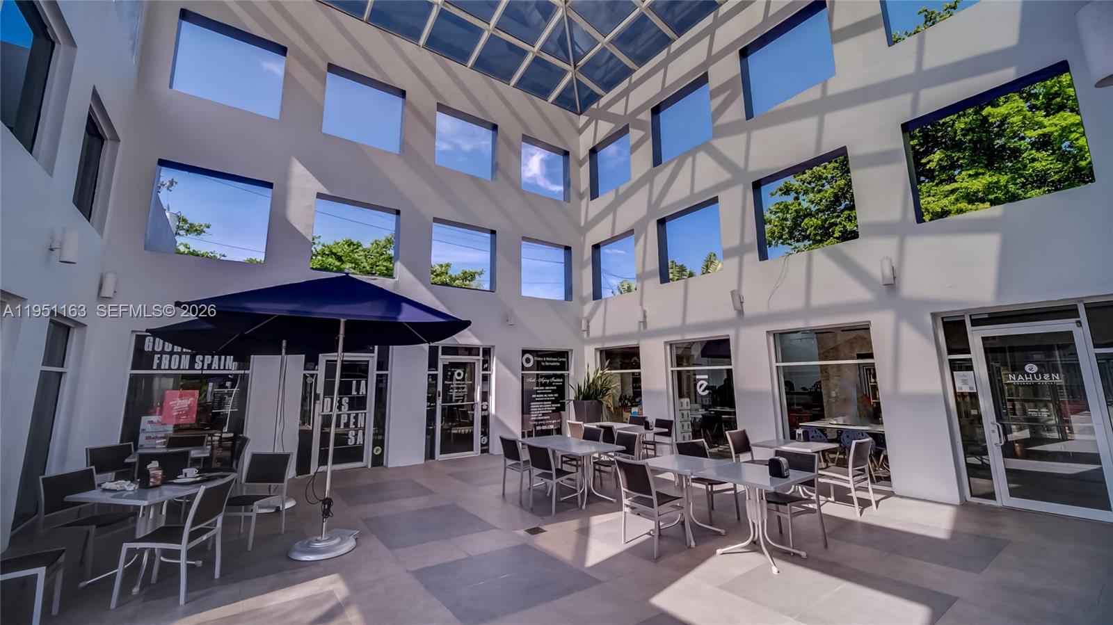 An outdoor courtyard features a glass atrium roof, white walls, and several tables with chairs — 260 Crandon Blvd # E18, Key Biscayne FL 33149, KEY BISCAYNE, FL