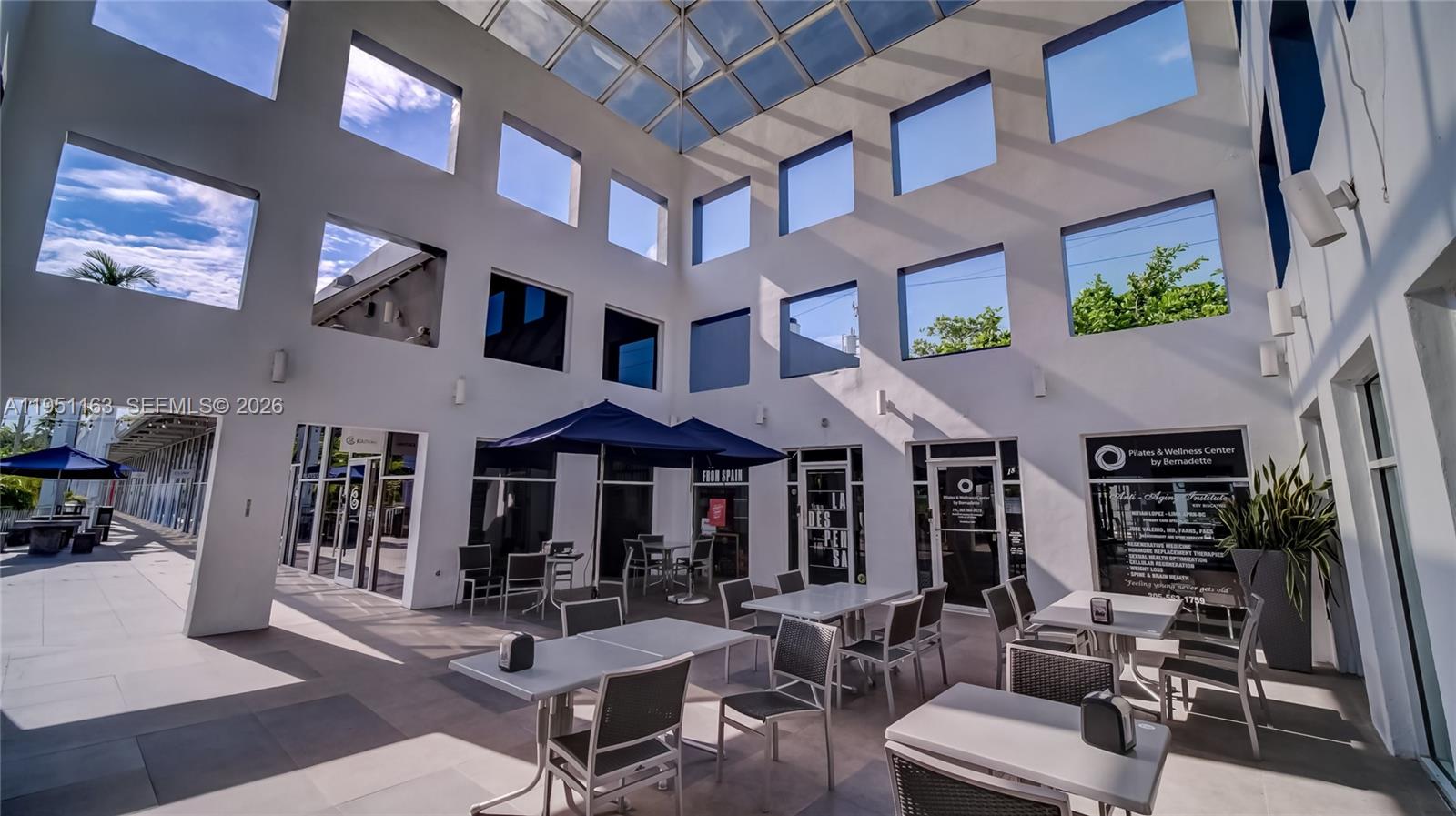 An outdoor courtyard features white walls, a glass roof, and several tables with chairs — 260 Crandon Blvd # E18, Key Biscayne FL 33149, KEY BISCAYNE, FL