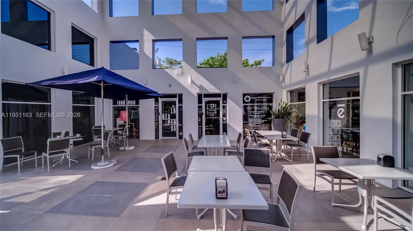 An outdoor courtyard features multiple dining tables with chairs under a blue umbrella — 260 Crandon Blvd # E18, Key Biscayne FL 33149, KEY BISCAYNE, FL