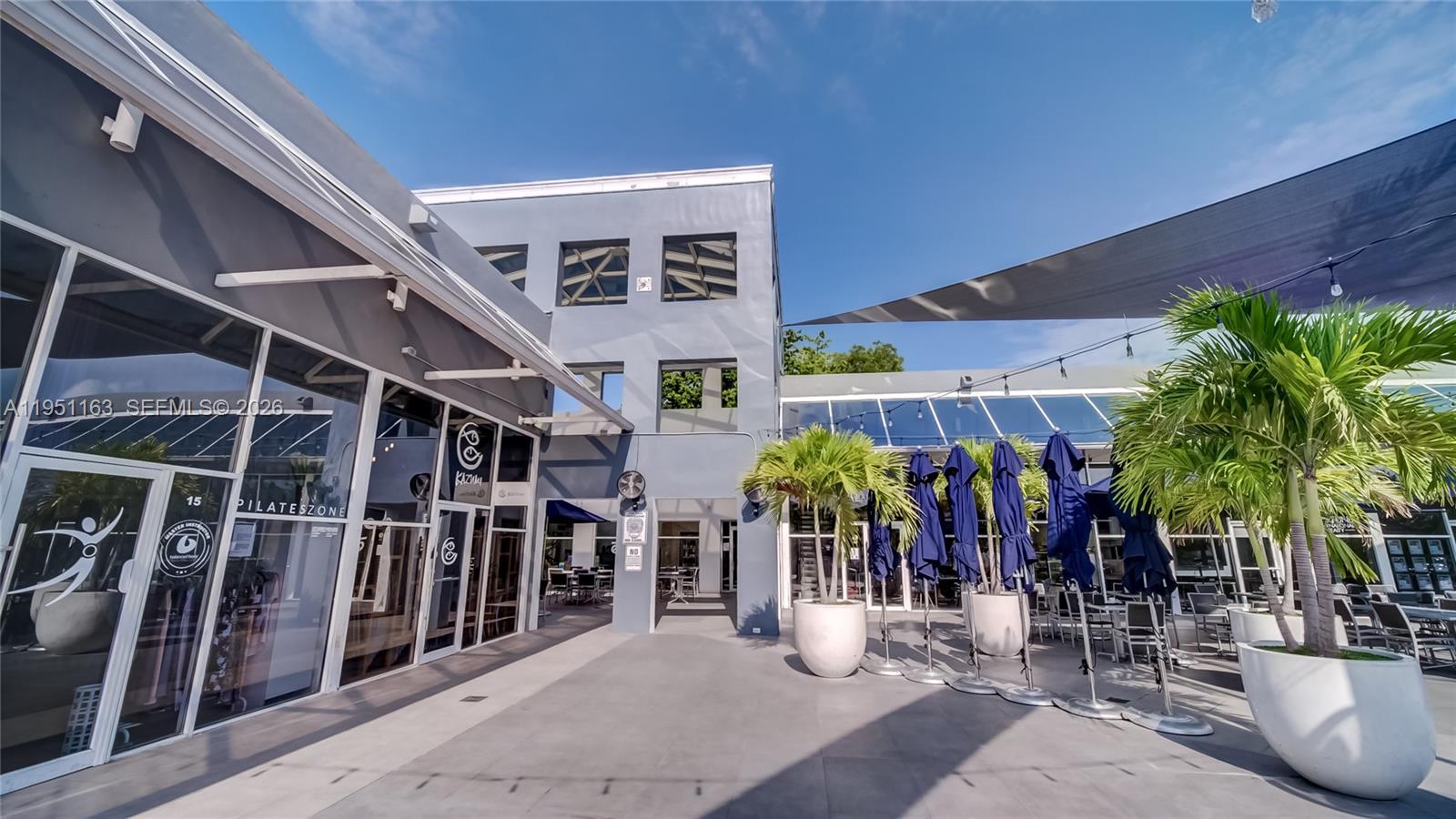 An outdoor patio area features a gray building, potted palm trees, and blue patio umbrellas — 260 Crandon Blvd # E18, Key Biscayne FL 33149, KEY BISCAYNE, FL
