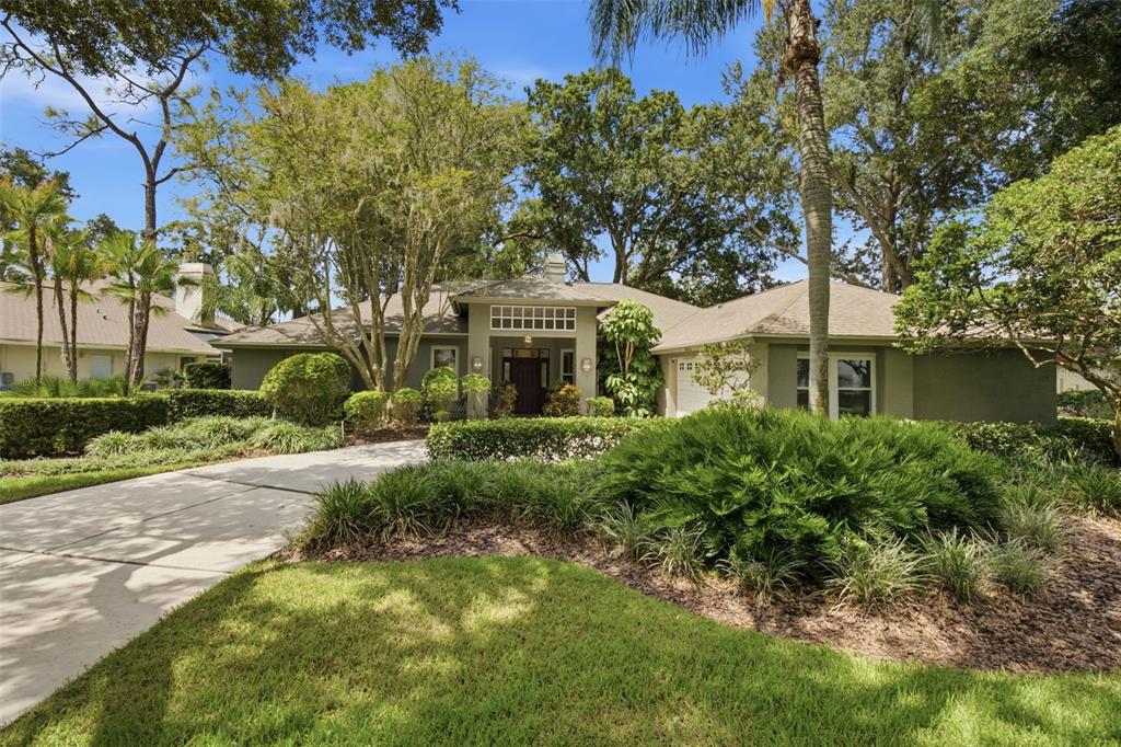 A single-story house with a concrete driveway, manicured landscaping, and mature trees in the yard — 16416 WINDSOR PARK DRIVE, LUTZ, FL