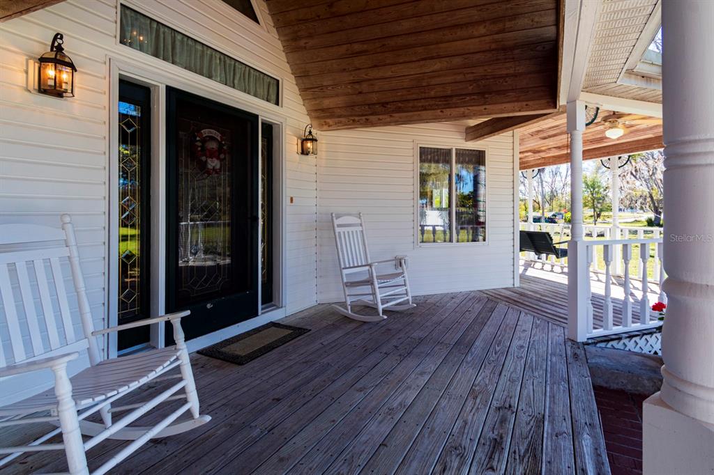 A covered wooden porch features two white rocking chairs, a front door, and railings — 9215 RIDGE ROAD, NEW PORT RICHEY, FL