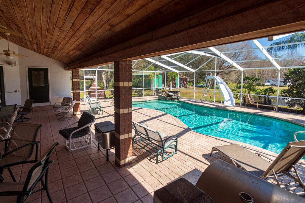 A covered patio with tile flooring overlooks a screened-in swimming pool with a slide — 9215 RIDGE ROAD, NEW PORT RICHEY, FL