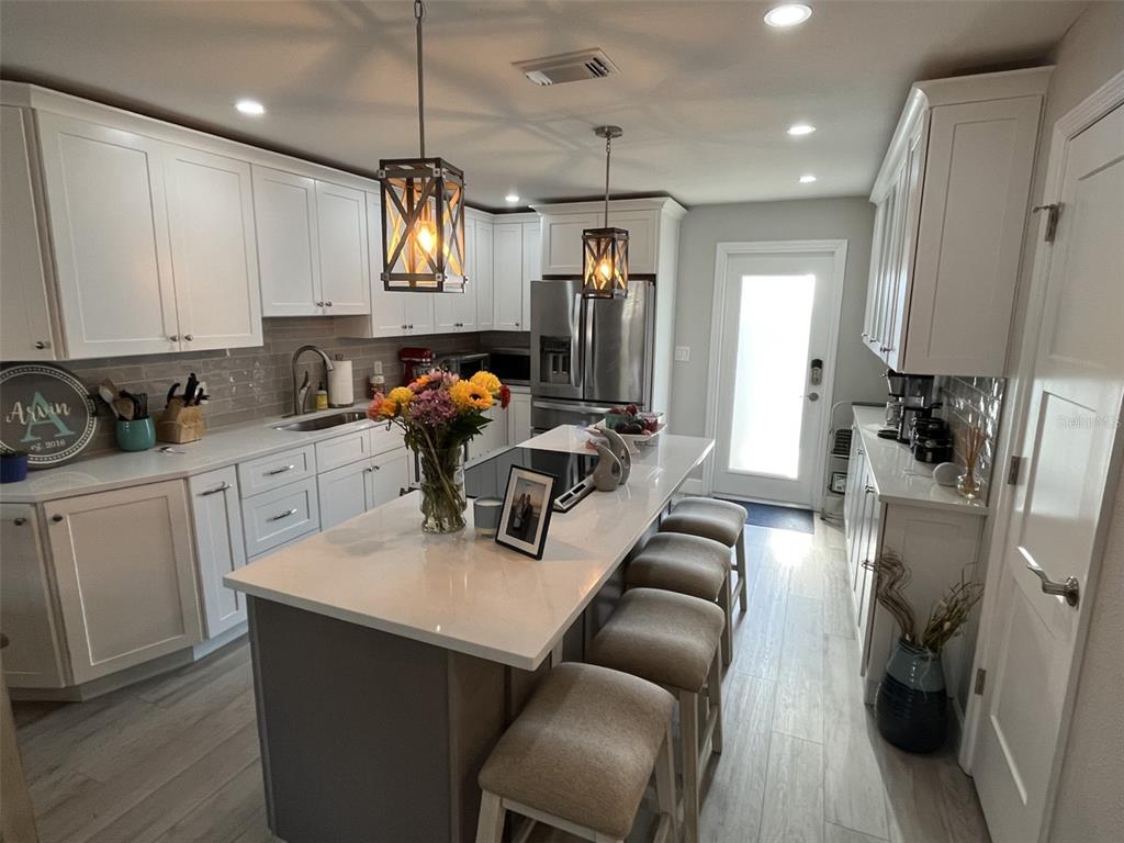 A kitchen features white cabinets, a central island with bar seating, and stainless steel appliances — 2369 19TH AVENUE SW UNIT B, LARGO, FL
