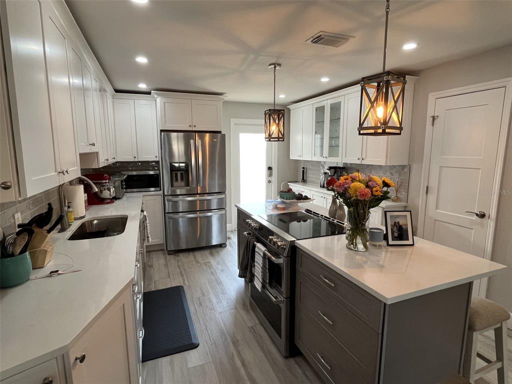 A kitchen features white cabinetry, a gray island, stainless steel appliances, and wood-look tile flooring — 2369 19TH AVENUE SW UNIT B, LARGO, FL